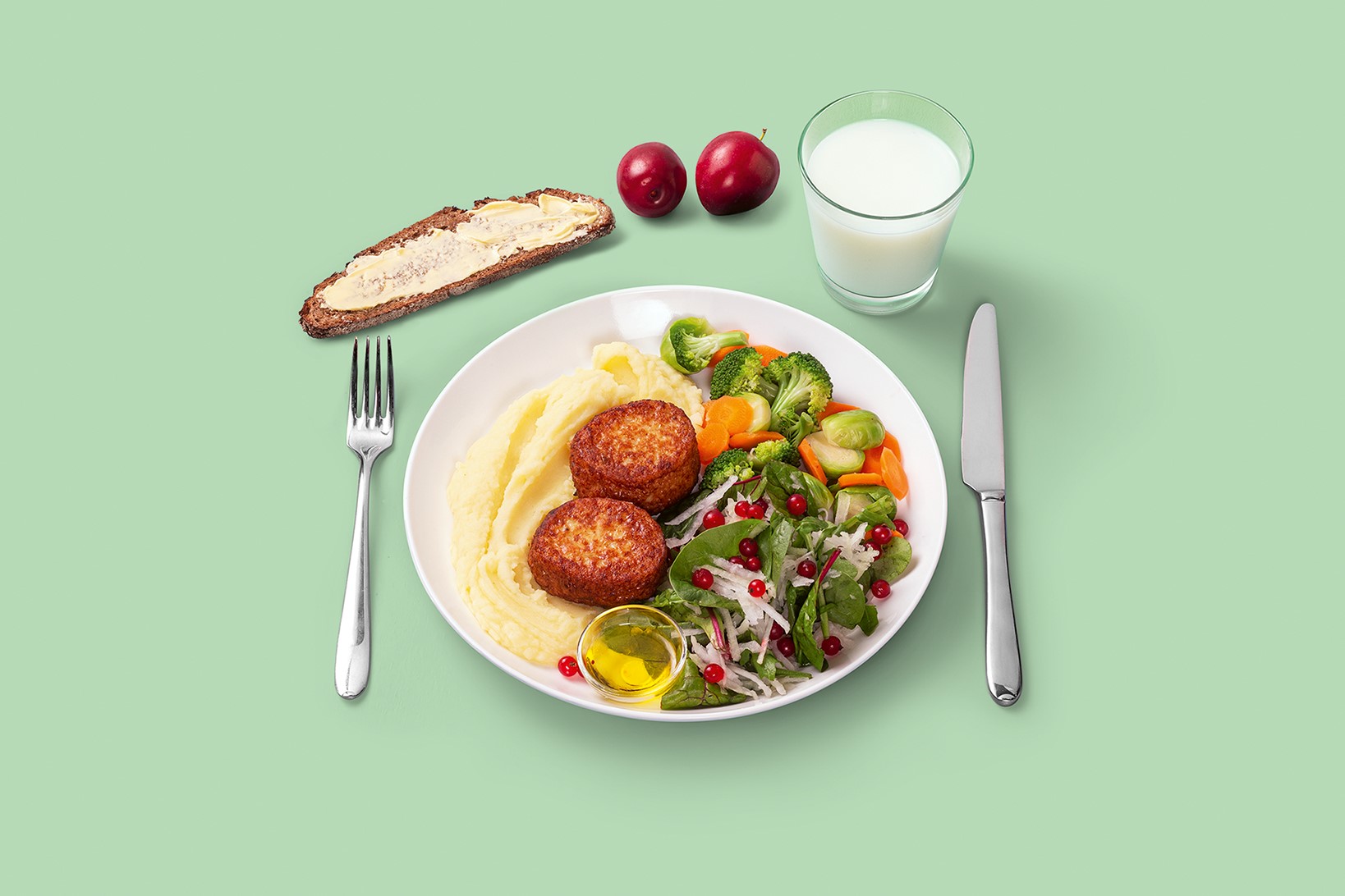 Kuvassa lautasmallin mukainen ateria, jossa kalapihvej&auml;, perunamuusia, kasviksia. Ruokajuomana rasvatonta maitoa tai t&auml;ydennetty&auml; kasvijuomaa, kasviksia ja &ouml;ljypohjainen salaatinkastike, t&auml;ysjyv&auml;leip&auml; levitteell&auml; ja luumuja j&auml;lkiruokana.